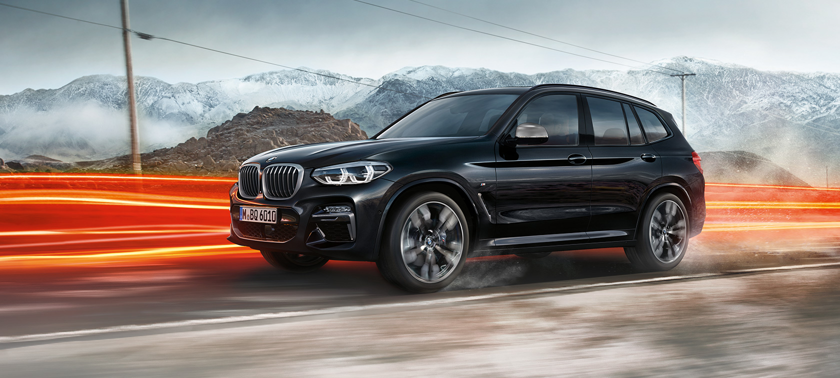 BMW X3 M40i ja BMW X3 M40d, metalliväri Sapphire Black, ajaa, ulkopuoli, sivunäkymä ja valot vuoristomaiseman edessä.