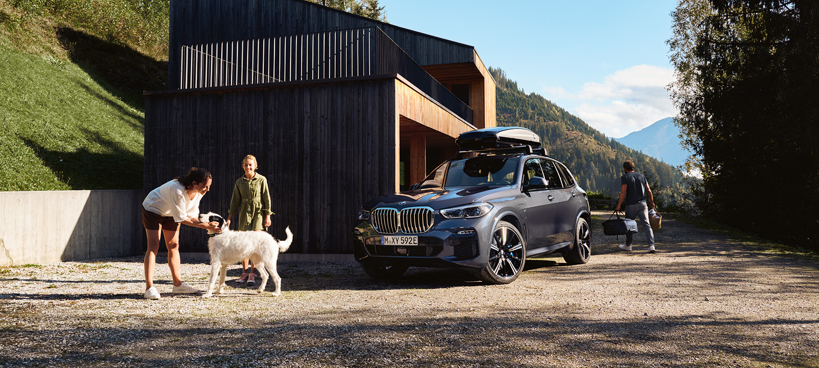 Perhe koiran kanssa BMW:n edessä parkkipaikalla kesäisessä ympäristössä. 